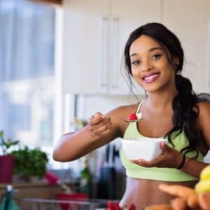 A young woman in workout clothes eating a bowl of fruit.